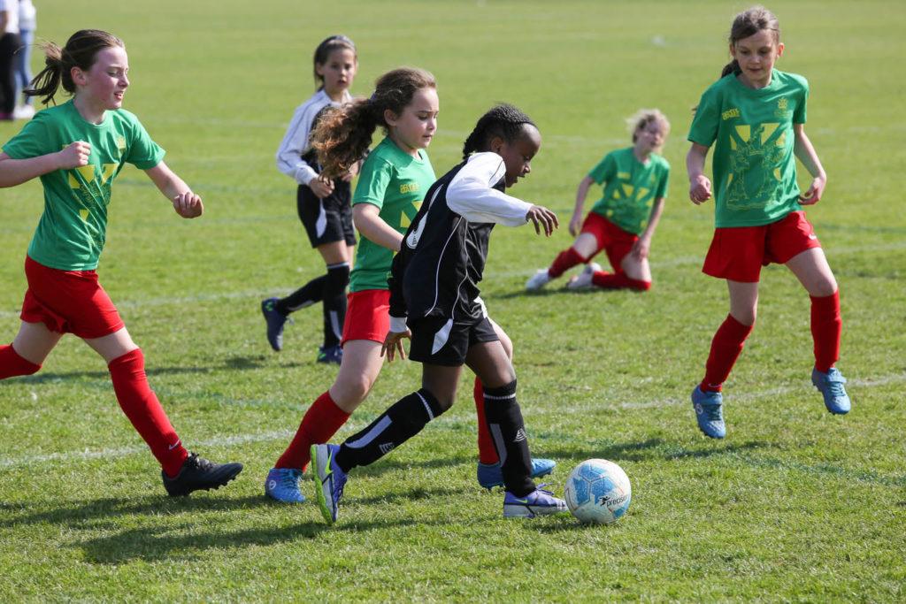 Young girls playing soccer on a field. They are running, kicking the ball, and enjoying the game with smiles on their faces.