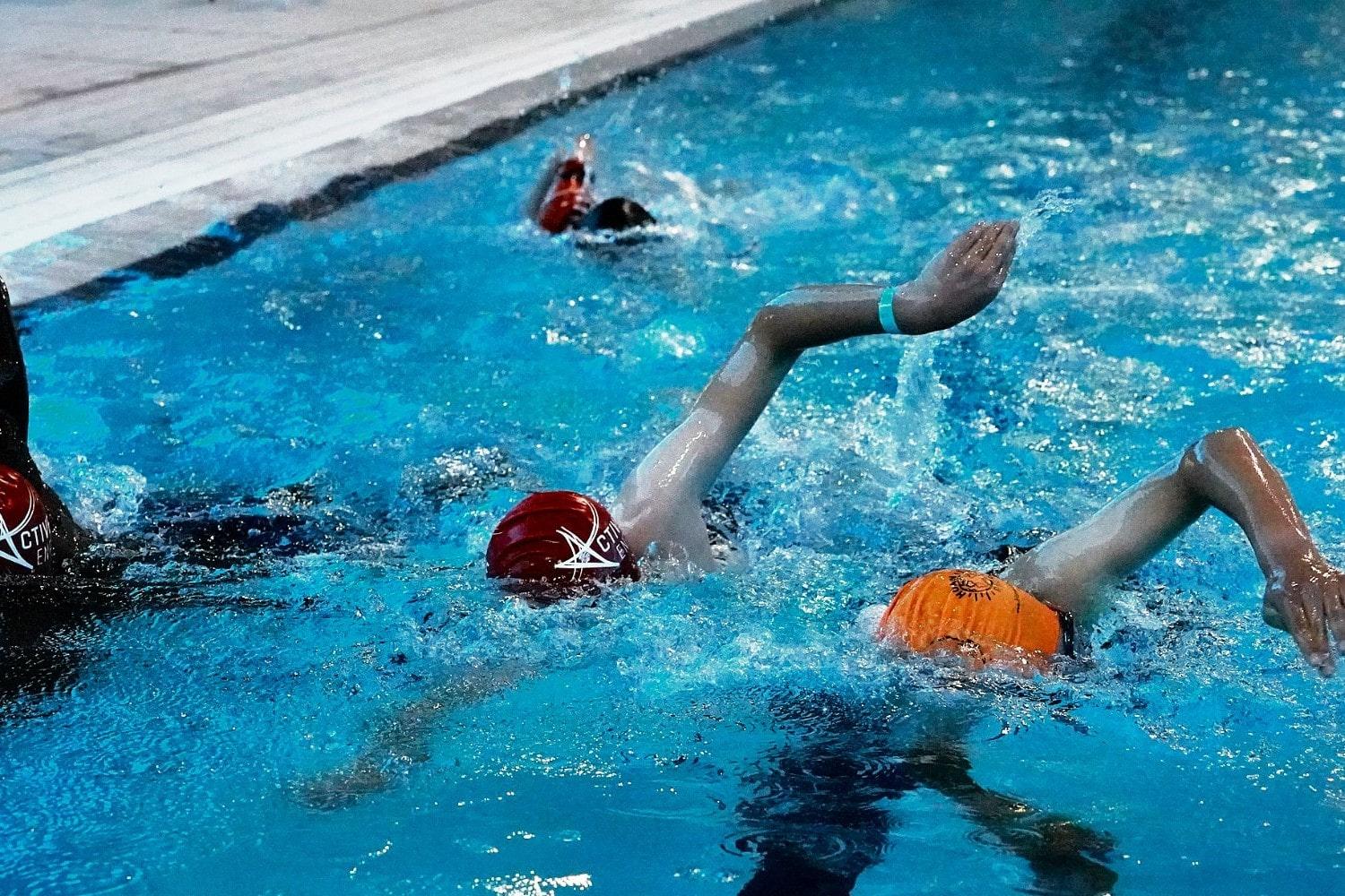 Competitive swimming race with swimmers in lanes, splashing water, and reaching for the finish line.