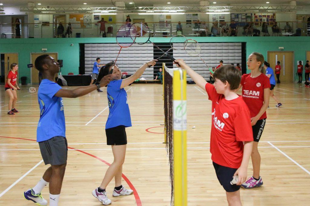 Young people playing badminton in an indoor gym.