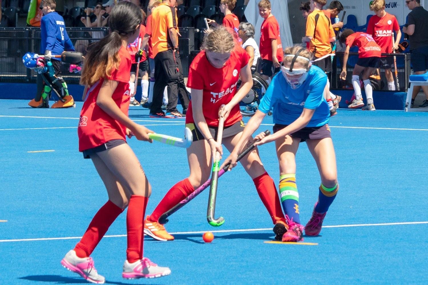 Several girls playing field hockey on a blue field.