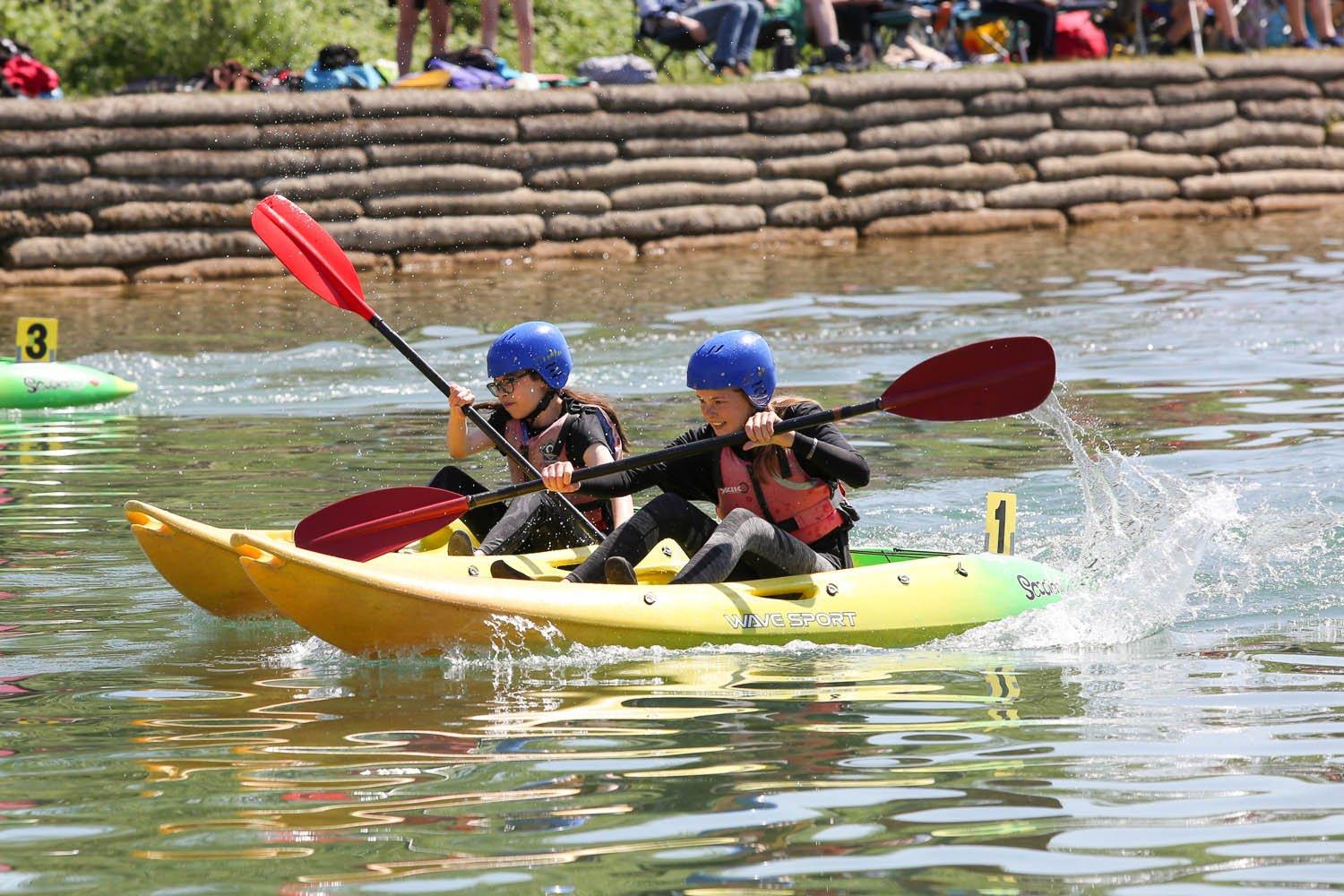 Two people paddling kayaks on a serene lake.