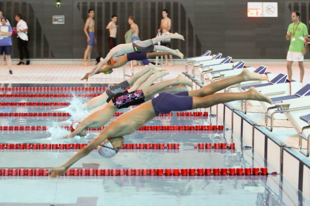 Swimmers diving into the pool at a competition, showcasing their swimming jump skills.