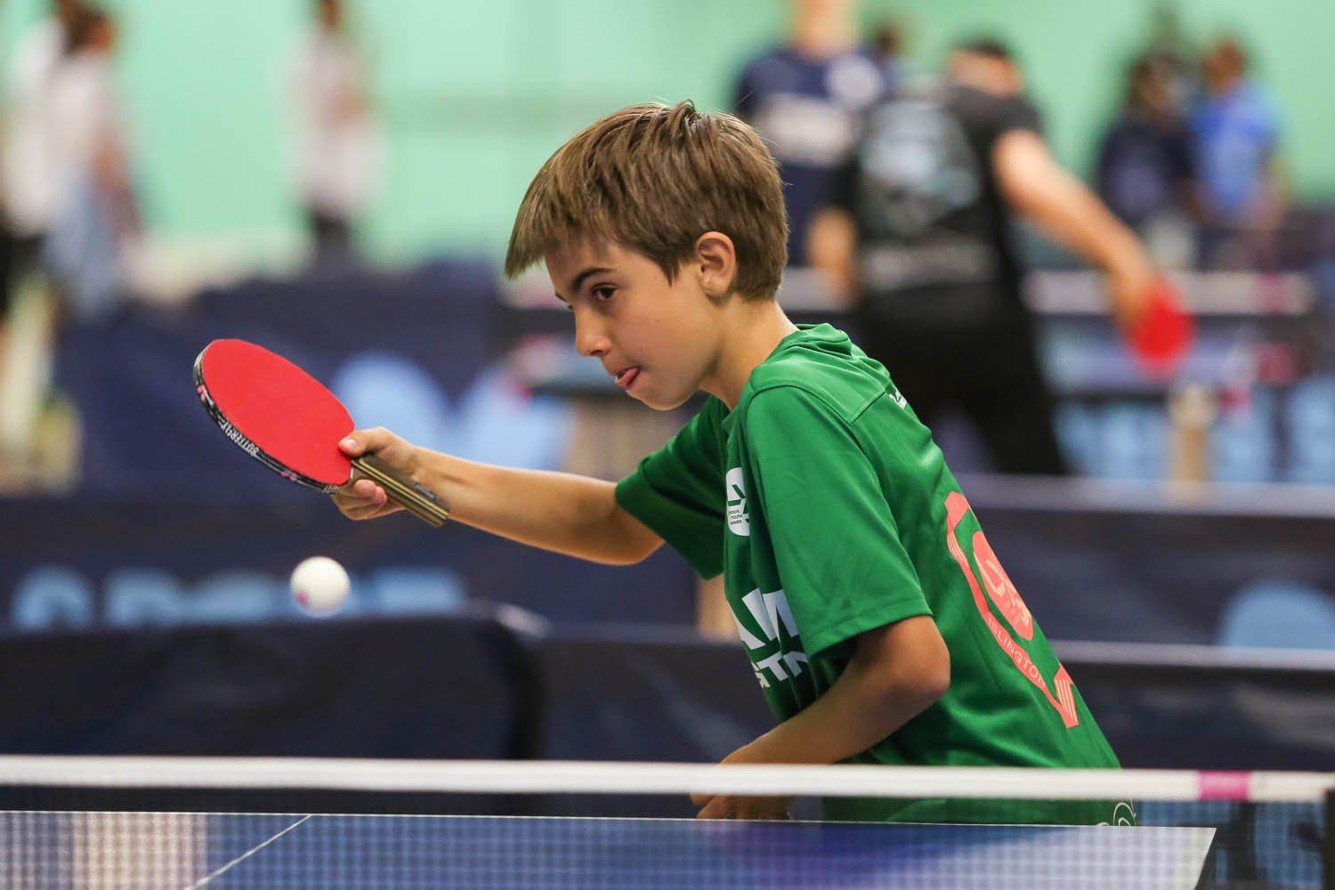 A young boy enthusiastically playing ping pong with a ball, showcasing his skills and passion for the sport.