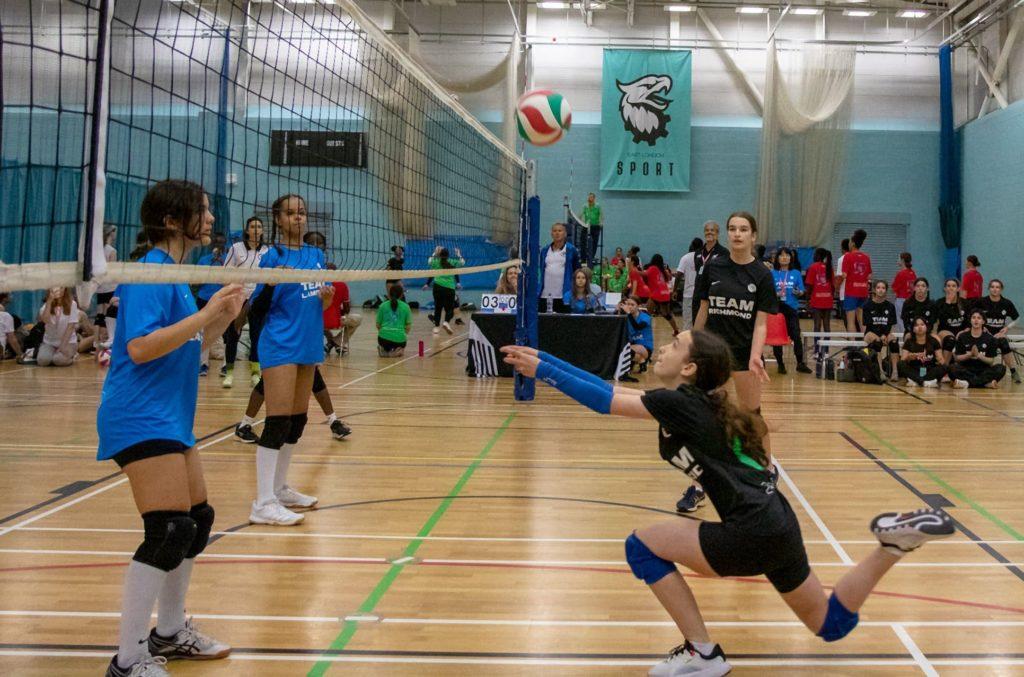 A girl stretching to catch a volleyball during a game.