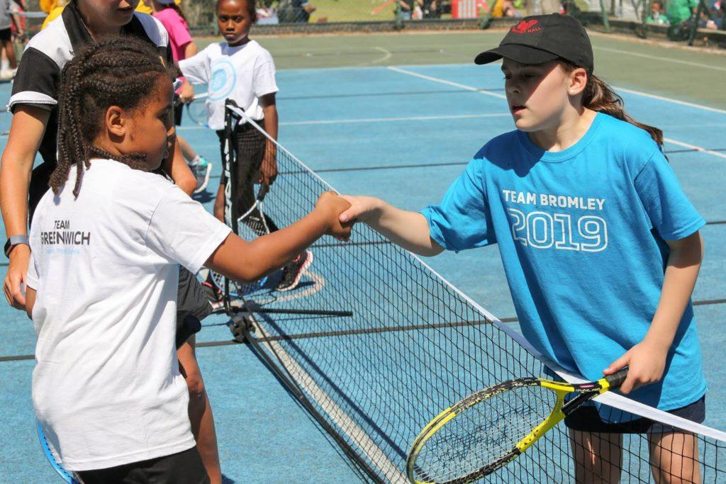 Two young girls shaking hands on a tennis court.