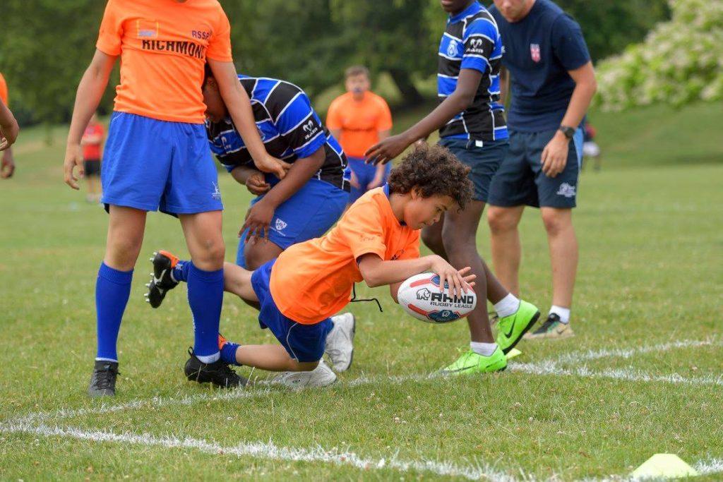 A young boy diving for a rugby ball during a wallyball game played indoors.