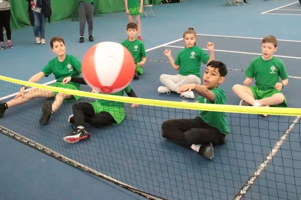 Two players in a wallyball court, hitting the ball over the net, surrounded by indoor walls.