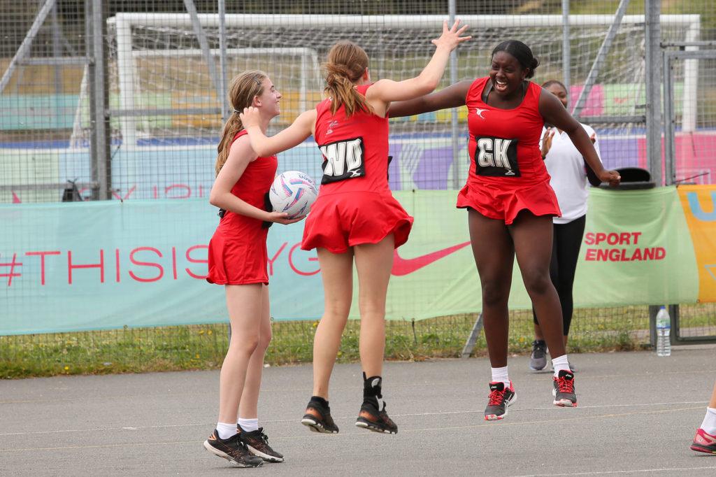 2 white girls and 1 black girl jump after winning LYG netball event