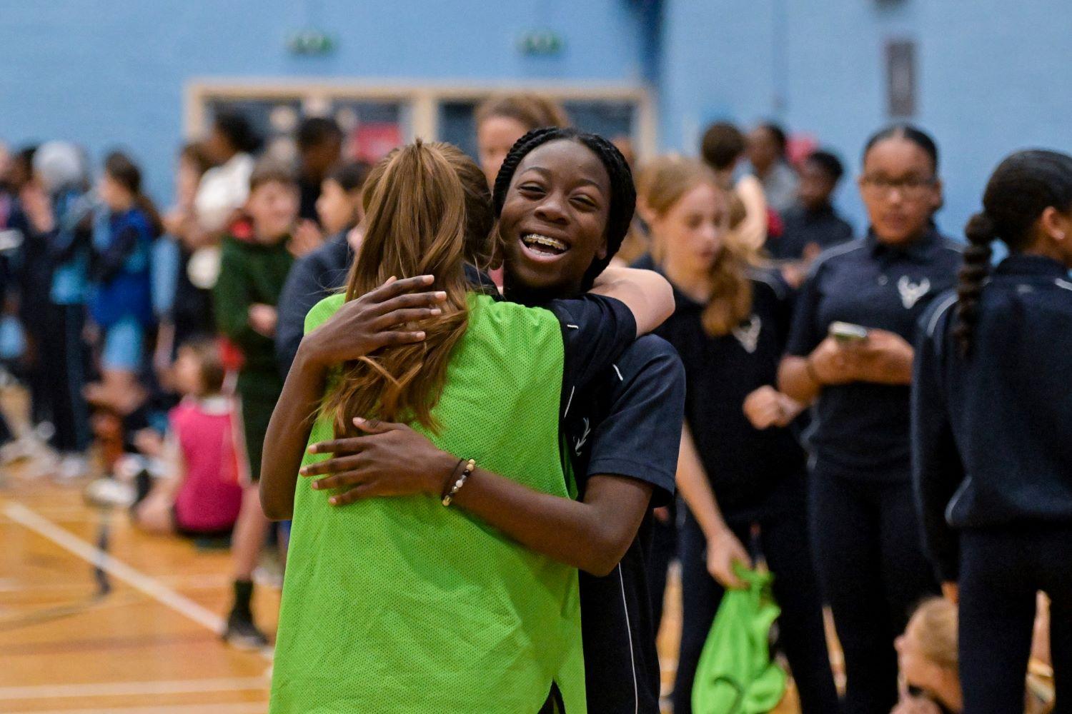 Two young women embracing in a gymnasium.