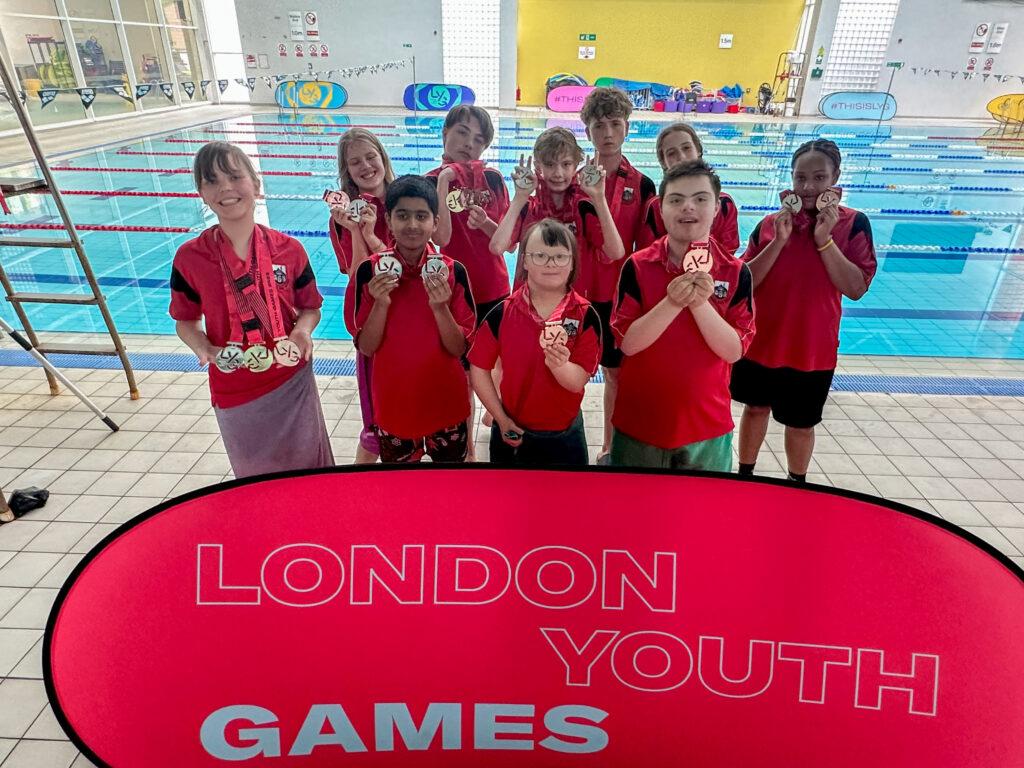 boys and girls smile with medals in front of pool