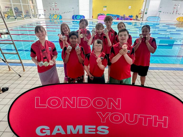 boys and girls smile with medals in front of pool