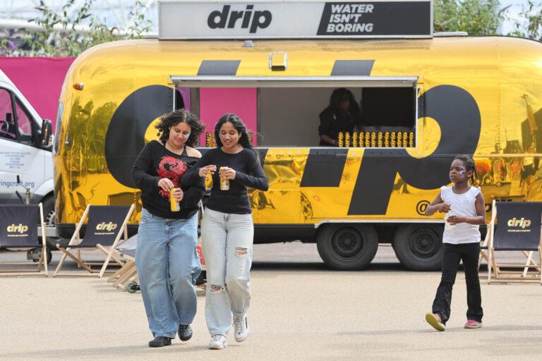 gold drip mobile trailer with 2 brown skin girls smiling holding cans