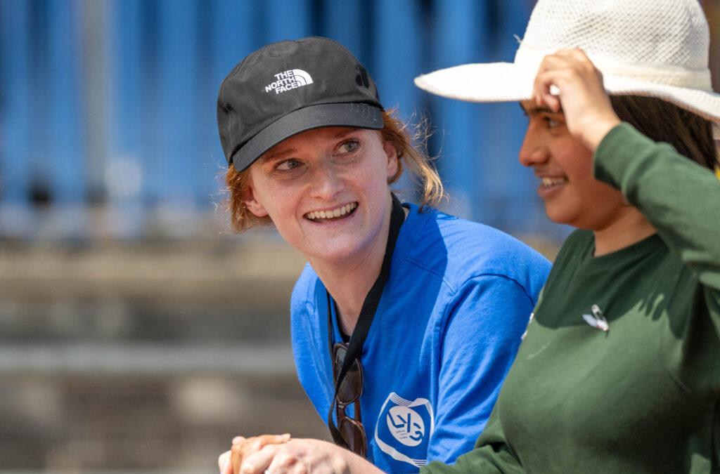 white female smiles at brown skin person wearing hat