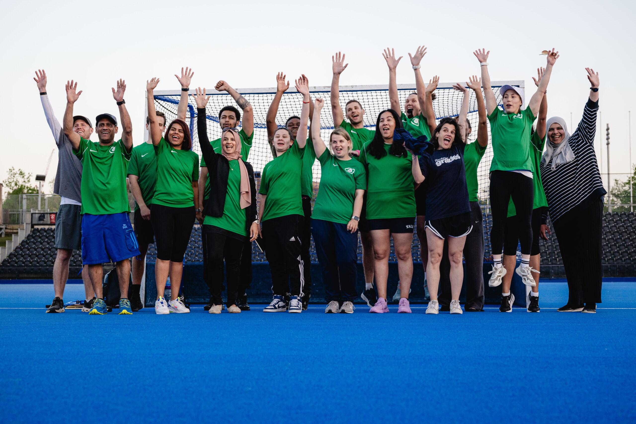 males and females in green shirts smile and wave arms in air
