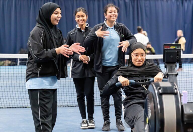 4 girls , one doing rowing, 3 girls cheering